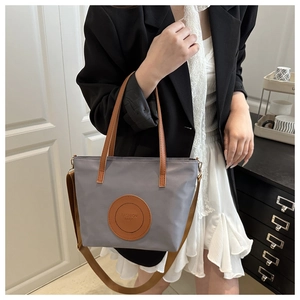 Detail of grey nylon tote bag showing brown leather straps and fashion bags logo patch