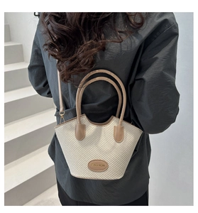 Detail of a woven bucket bag featuring tan leather trim and an adjustable shoulder strap