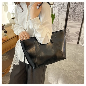 Detail of a large black glossy leather tote bag with long shoulder straps for daily commute