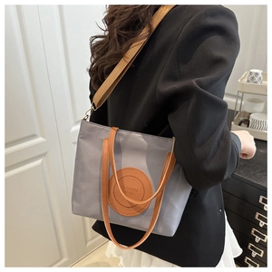 Detail of grey nylon tote bag with brown leather patch and wide textile shoulder strap