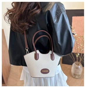 Model wearing a small woven bucket bag in cream and brown leather with shoulder strap