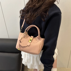 Sac seau rose en cuir grainé avec fermoir doré et charm de chien porté par un mannequin
