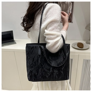 Detail of a large black tote bag featuring a glossy pleated texture and slim shoulder straps