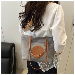 Detailed back view of a grey tote bag featuring brown leather handles and woven shoulder strap