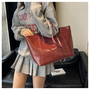 Deep burgundy large tote bag in glossy faux leather worn over the shoulder by a model