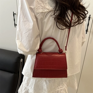 Red crocodile texture crossbody bag with unique knot handle shown on model's side