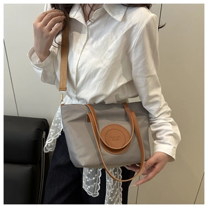 Detail view of the gray fabric tote bag with brown leather handles and wide shoulder strap