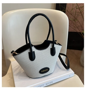 Close-up of straw bucket bag with black leather trim and gold fashion lettering