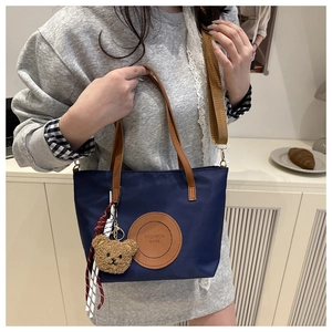 Detail of navy nylon tote bag with brown leather patch and cute teddy bear charm
