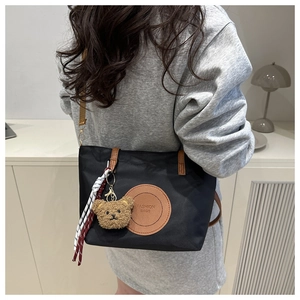 Detail of black nylon tote bag with brown leather straps and cute plush bear accessory