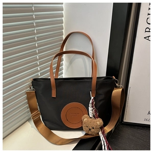 Detail of black nylon tote with leather strap and a cute brown plush bear charm