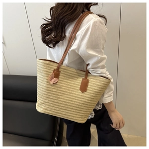 Detail of hand-woven straw tote with brown leather straps and pink butterfly charm