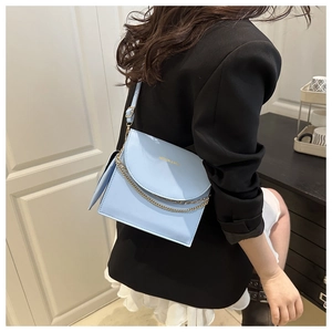 Detail of light blue crossbody bag with gold lettering and adjustable chain strap on model