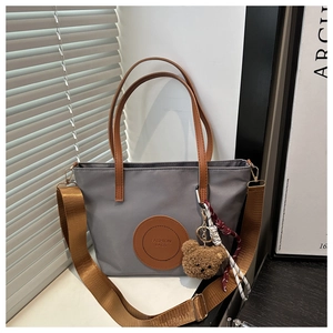 Detail of grey nylon tote bag featuring brown straps, fashion patch and a plush bear charm