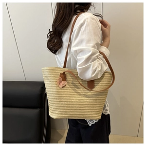 Detail of hand-woven straw tote bag featuring brown leather straps and pink charm