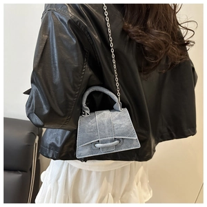 Detail of grey denim trapezoid bag with silver chain strap and curved bottom base