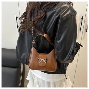 Detail of a brown mini handbag with silver metal bow and shiny leather texture