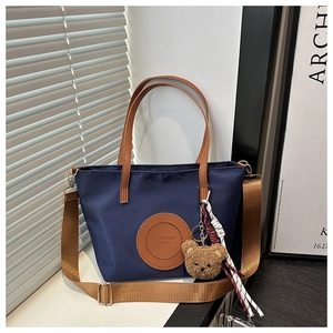 Detail of navy nylon tote bag with brown PU straps and a cute plush bear accessory