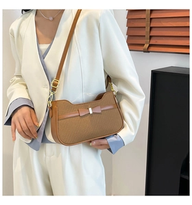 Detail of a brown woven texture shoulder bag featuring a leather bow and metal buckle
