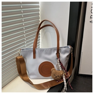 Detail of grey nylon tote bag with brown leather handles and plush bear charm decoration