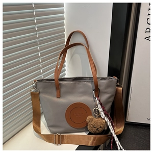 Detail of grey nylon tote bag with brown leather handles, fashion tag and cute bear charm