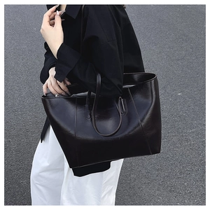 Detailed view of large black glossy leather tote bag with double handles in street setting