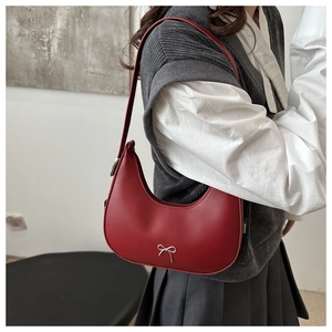 Detail showing burgundy crescent shoulder bag with silver metallic bow on leather