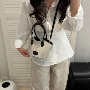 Minimalist beige woven bucket bag with contrast black handles and fashion tag on display