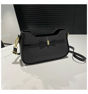 Detail of black woven crossbody bag featuring a leather bow and gold metal buckle