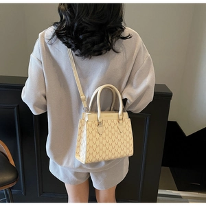 Detail of beige square bag with M-letter jacquard and cream leather handles in use