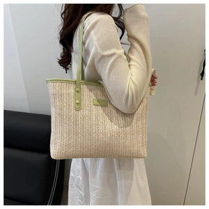 Close-up of beige woven texture and green leather trim detail on a straw tote bag