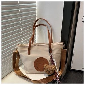 Detail of cream nylon tote bag with brown leather handles and plush bear charm accessory