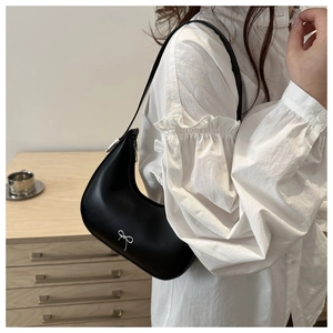 Close-up of black crescent hobo bag with silver bow detail on white ruffled shirt