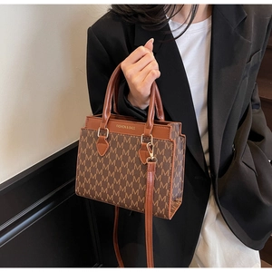 Detail showing the brown letter M print and leather handles of the square crossbody bag