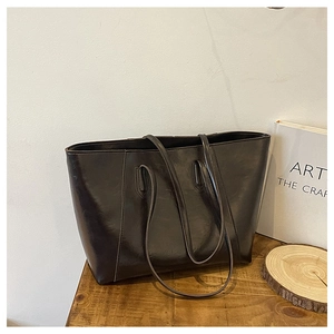 Close-up of black glossy leather tote bag with fine stitching on a wooden surface