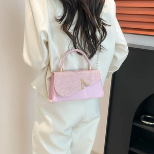 Pink glitter square crossbody bag with gold V logo and chain strap worn by a model