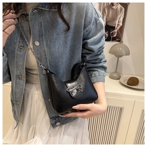 Détail d'un sac hobo noir avec boucle nœud argentée et chaîne sur une tenue élégante