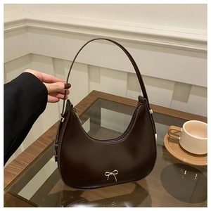 Close-up of dark brown crescent bag with silver metallic bow detail on a cafe table
