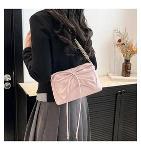 Pink crossbody bag with large bow detail and gold chain strap shown on a model