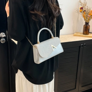 Minimalist white and silver square crossbody bag with metallic V buckle worn by model