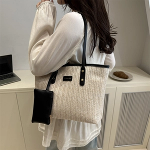 Beige woven tote bag with black leather handles shown on shoulder with small pouch