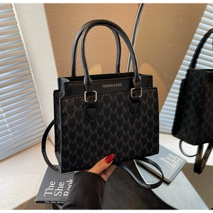 Detail of a chic black square handbag featuring embossed M-pattern and gold lettering