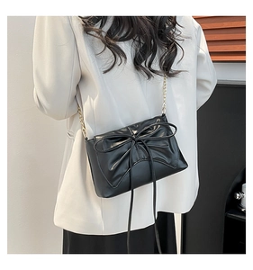 Detail of black tote bag with oversized bow and elegant gold chain strap worn by model