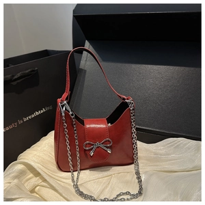 Détail d'un sac demi-lune rouge avec nœud en métal sur fond de satin crème