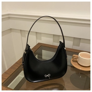 Close-up of black crescent underarm bag with silver bow buckle on glass table