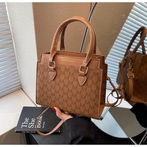 Detail of trendy brown crossbody square bag with M-letter monogram pattern and round handle