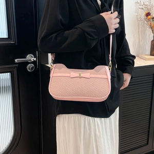 Pink woven handbag with leather bow detail and shoulder strap shown on a model