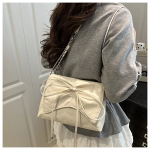 Détail du grand nœud sur le sac à bandoulière crème porté par un mannequin en scène