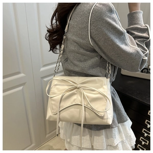 Détail d'un sac bandoulière beige avec nœud décoratif et bandoulière chaîne sur un mannequin