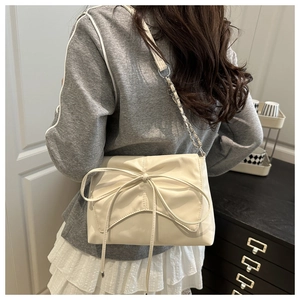 Détail du sac en similicuir crème avec grand nœud décoratif et bandoulière en chaîne